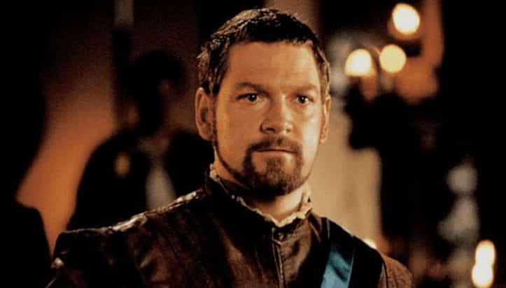 Kenneth Brannagh looking at the camera in brown tunic as Iago about to speak his 